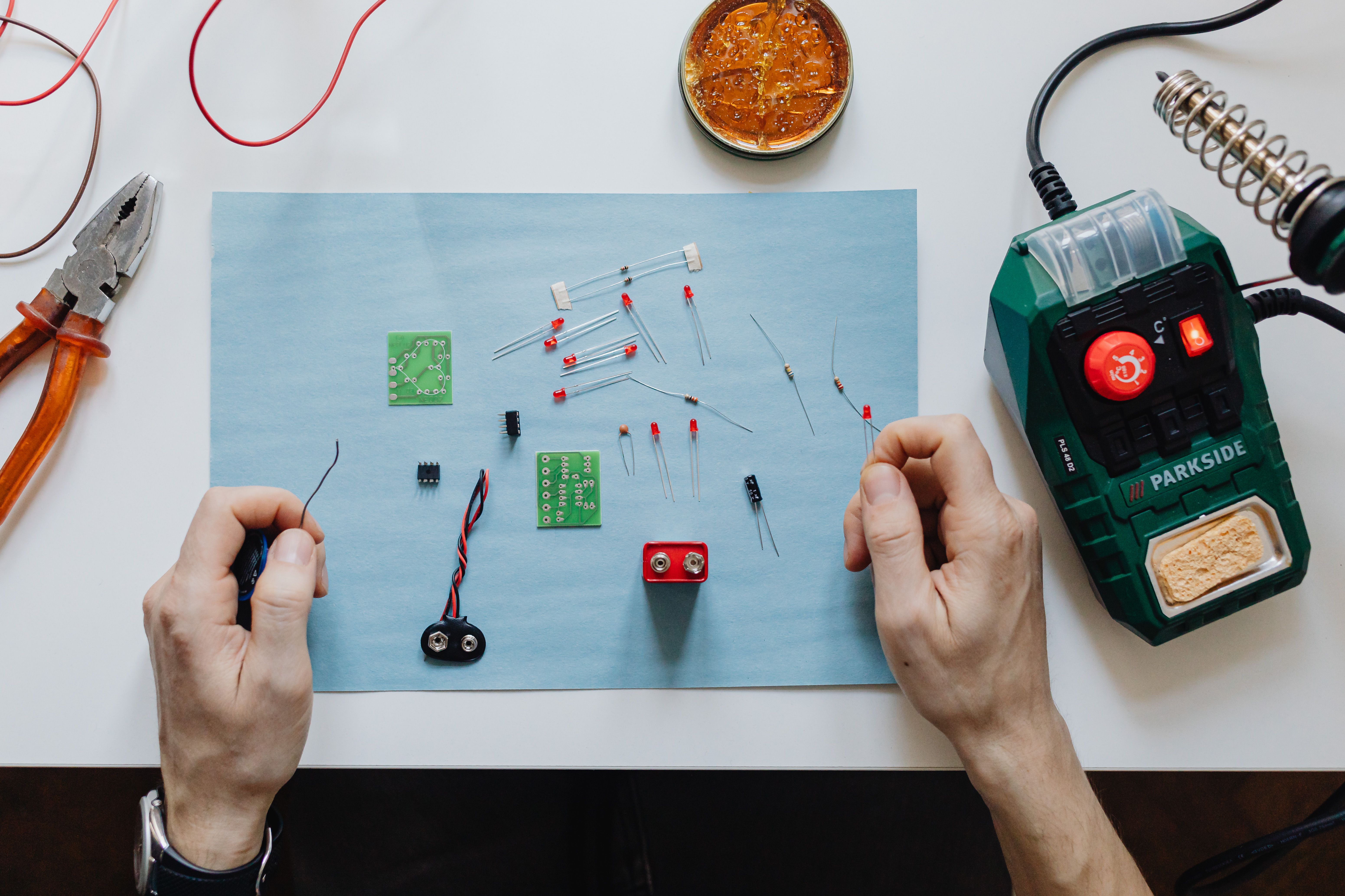 Hands repairing a circuit board with tools at a workbench, illustrating the assembly and soldering stages of the project.